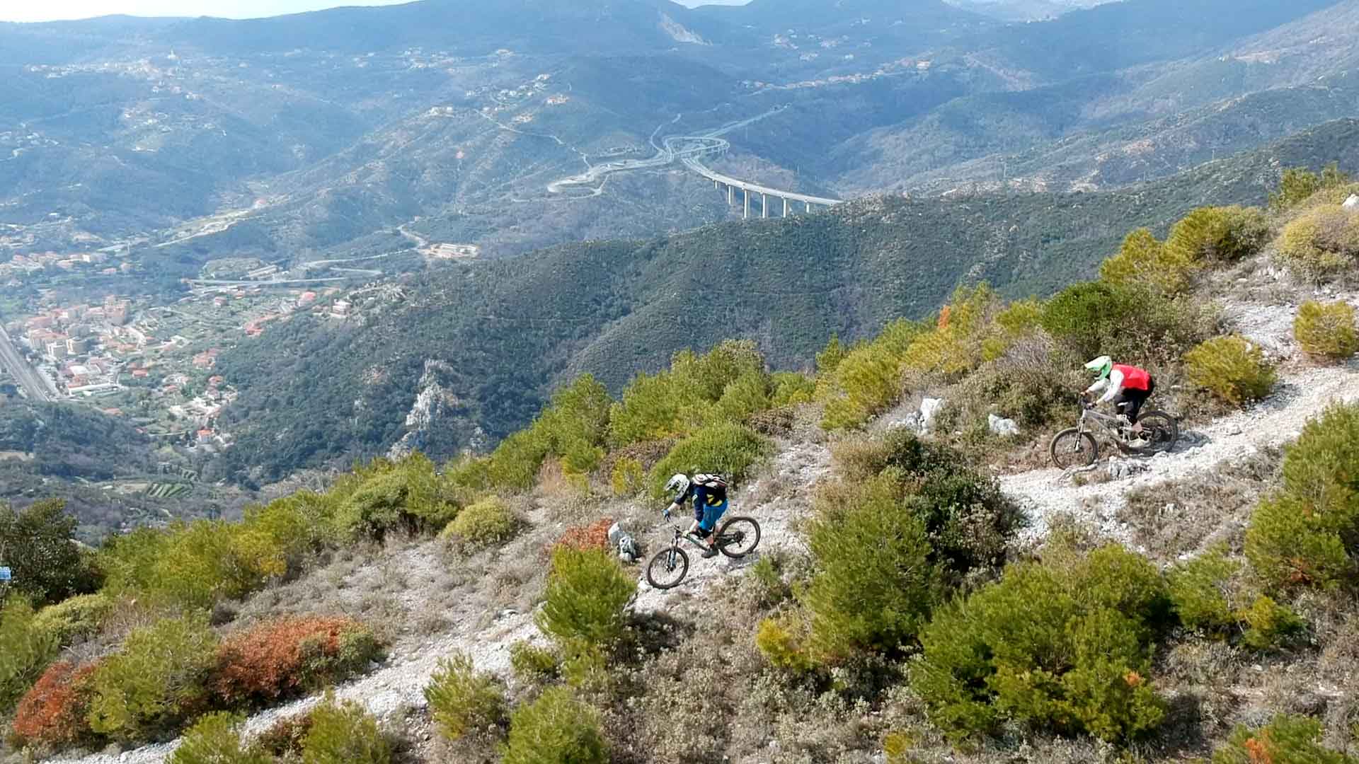 2 bikers rijden over een berg rug met finale ligure op de achtergrond