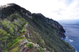 2 mountainbikers rijden over een ridgeline. de steile bergwand mond uit in de zee.