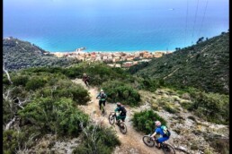 IN een treintje rijden de mountainbikers over een trail. Het uitzicht is op de prachtige azuur blauwe zee bij finale ligure