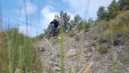 een mountainbiker rijdt door een bocht over een trail vol stenen.